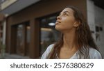 Woman looking thoughtful standing on an urban street during daytime, featuring a young, beautiful, mixed-race, brunette woman with a pensive expression in a city setting