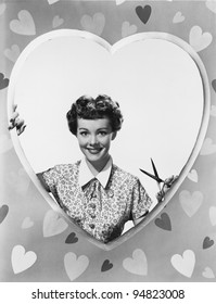 Woman looking through heart shape with scissors