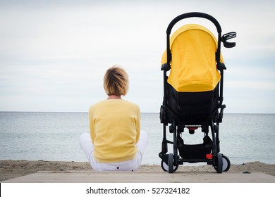 Woman looking through the sea while sitting on beach with baby carriage. Young mother sitting outdoor with stroller. Maternity concept with copyspace