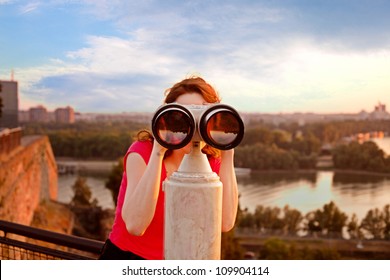 woman looking through sightseeing  binoculars on Belgrade Fortress sky, river and city in background