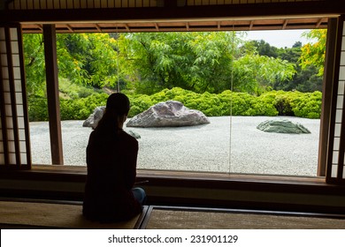 Woman Looking Through A Window At A Japanese Zen Rock Garden.