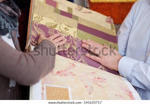 Woman looking at wallpaper and fabric swatches
holding a sample book in her hands while discussing them with a
male partner or salesman