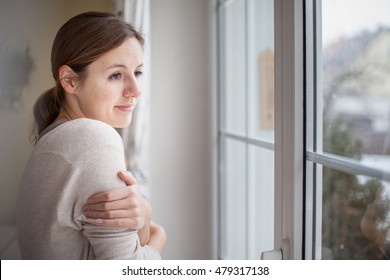 Woman Looking From A Window Of Her House On A Cold And Snowy Winter Day