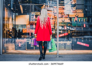 Woman looking at window shop - Young pretty girl standing in front of a boutique holding shopping paperbags