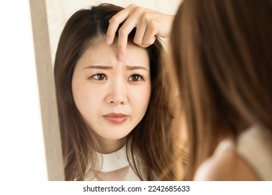 A woman looking at the wrinkles between her eyebrows in the mirror. - Shutterstock ID 2242685633