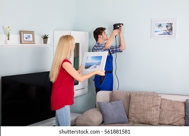 Woman Looking At Young Man Using Power Drill On White Wall At Home