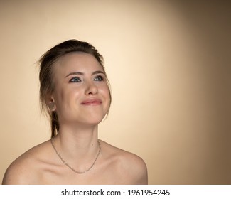 The Woman Looks Cheerfully In The Upper Right Corner. She Has A Strange Hairstyle, A Plug In Her Ear, A Piercing In Her Nose, And A Silver Earring On Her Neck. Studio Photography, Beige Background