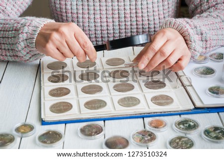 Woman looks at the coins through a magnifying glass
