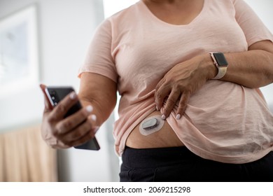 Woman Looks At Diabetes Health And Glucose Data On Smartphone While Wearing A Continuous Glucose Monitor (CGM) On Her Abdomen.