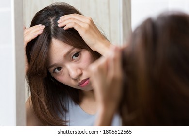 A Woman Looks At Her Scalp In The Mirror.