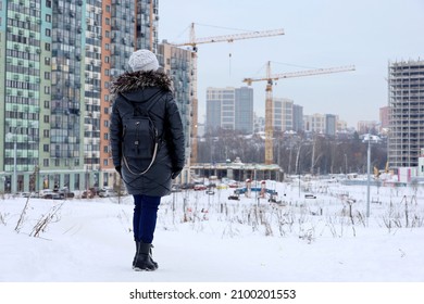 Woman looks at the houses under construction, urban landscape in winter. Building industry and real estate concept