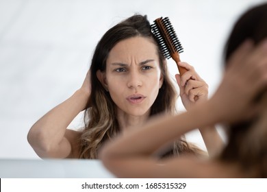 Woman looks in mirror feels dissatisfied by hairstyle, hair condition, holds hairbrush combing hair, hairloss problems vitamin deficiency sign, blow-dryer straightener overuse, need treatment concept
