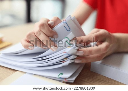 Woman looks for necessary accounting materials flipping stapled documents. Female secretary sits at wooden table doing paperwork in modern office
