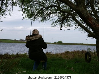 Woman looks out onto lake sitting on swing wide shot selective focus