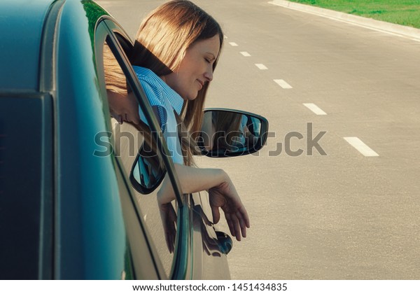 A woman looks out the\
window of the car. There\'s a road in the background. Travel and\
comfort