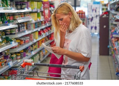 Woman looks shocked at a paper check in a grocery supermarket price increase and inflation. Upset woman in a supermarket viewing receipts looking at her shopping receipt and shocked about the price - Shutterstock ID 2177608533
