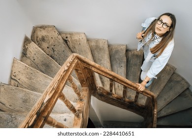 A woman looks up standing on an old wooden staircase. - Powered by Shutterstock