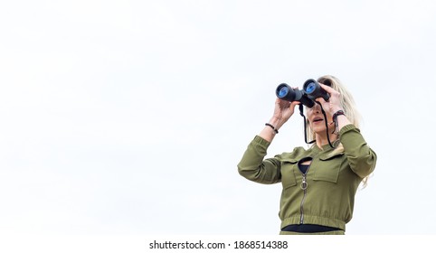 Woman looks through binoculars, standing in gray sky background. - Powered by Shutterstock