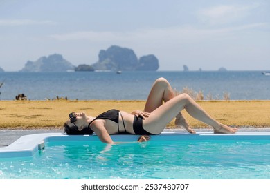 A woman lounges beside a sparkling pool, savoring the warm sun and breathtaking ocean landscape. She wears a black bikini and sunglasses, embodying a leisurely vacation vibe. - Powered by Shutterstock