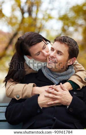 Woman in love kissing happy man in park on cheek