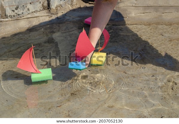 A woman lowers a toy sailboat into the pool. An\
adult woman\'s hand holds a toy made from a kitchen washcloth.\
Children\'s sailing regatta in the city fountain. Summer, daytime.\
Selective Focus.