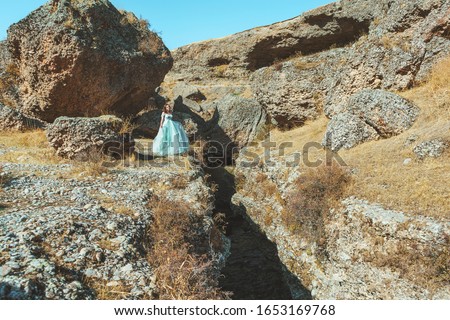 A woman in a lush beautiful mint dress in Aksu canyon on the background of a river in southern Kazakhstan. A young woman in an evening ball gown on a background of rocks and mountains. 