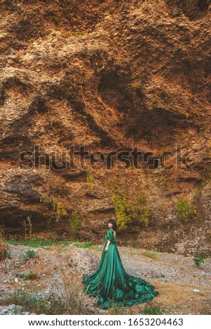 Woman in  lush green dress in Aksu canyon in southern Kazakhstan. Young woman in fairy tale evening ball gown on background of rocks and mountains. Beautiful girl in long dress in the mountains