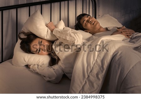 woman lying awake in bed, covering her ears to block out the sound of her partner snoring, capturing a common sleep disturbance [[stock_photo]] © 