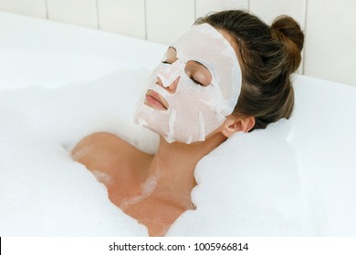 Woman lying in bathtub with a sheet mask on her face - Powered by Shutterstock