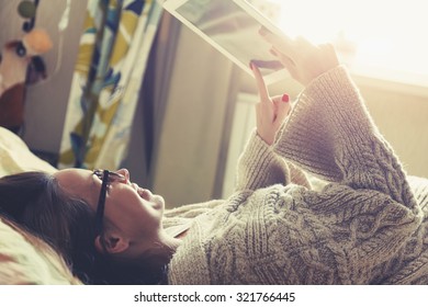 woman lying in bed with digital tablet touching with finger in morning sunlight - Powered by Shutterstock