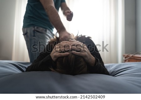 Woman lying in bed and protecting herself while her partner threatens to assault her.