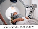 A woman lying down on a CT scan machine bed in a medical clinic, being attended to by a healthcare professional, ready for a diagnostic imaging procedure to evaluate internal organs.