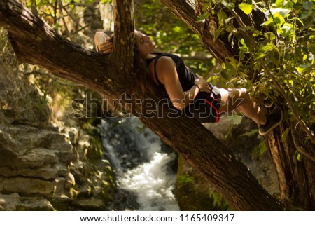 A woman lying down in a trunk over a lake with some waterfalls. 