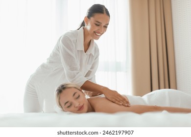 A woman is lying face down on a massage table while a massage therapist is applying pressure to her back in a spa setting, copy space - Powered by Shutterstock