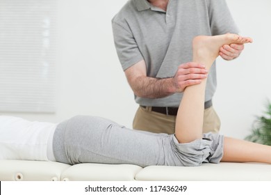 Frau, die vorn liegt, während eine Physiotherapeutin ihr Bein im Raum untersucht