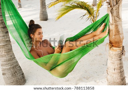 Woman is lying in hammock on the beach and using tablet PC