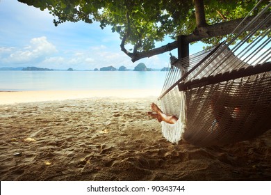 Woman lying in a hammock in tree's shadow on a beach