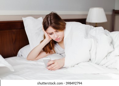 Woman lying on bed looking unhappy with a text message. - Shutterstock ID 398492794