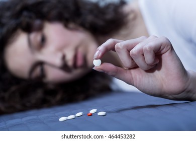 Woman lying on bed and looking at pill