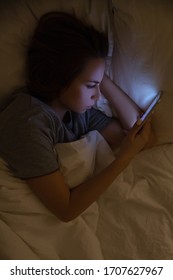 Woman Lying On Bed Using Mobile Phone  At Night, Reading Or Watching, Looking At Screen. Mobile Addiction, Nomophobia, Insomnia, Sleep Disorder Concept. Stress And Depression About News And Loneliness