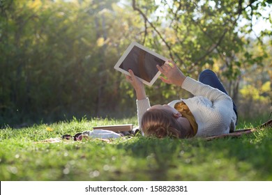 woman lying on bedding on green grass with tablet during picnic in the park