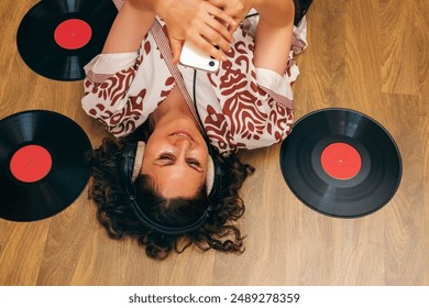 Woman lying on floor with headphones , vinyl records and phone.  - Powered by Shutterstock