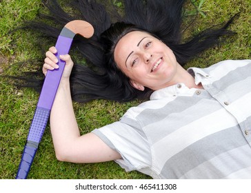 Woman lying on grass resting after playing hockey, holding hockey stick. - Powered by Shutterstock