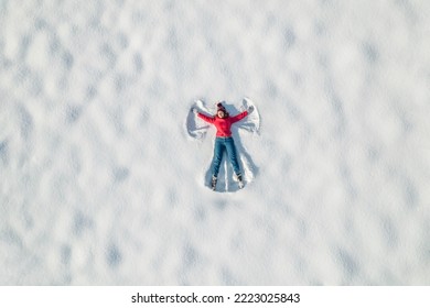 Woman lying on a snow and doing angel print on a snow covered land. Aerial, top view. Drone photo. Winter  - Powered by Shutterstock