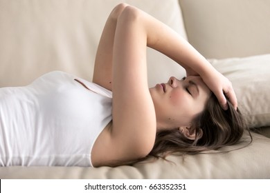 Woman lying on sofa having headache. Stressed girl suffering of fatigue, migraine, trying to cope with nervous tension, worries because of problems, unwanted pregnancy, negative thoughts and emotions
