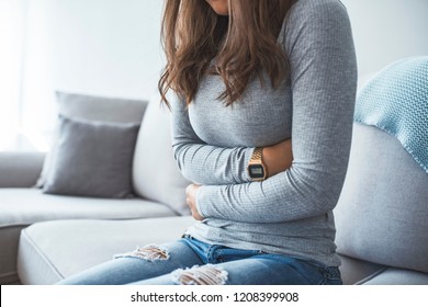 Woman lying on sofa looking sick in the living room. Beautiful young woman lying on bed and holding hands on her stomach. Woman having painful stomachache on bed, Menstrual period - Powered by Shutterstock