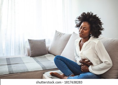 Woman lying on sofa looking sick in the living room. Beautiful young woman lying on bed and holding hands on her stomach. Woman having painful stomachache on bed, Menstrual period