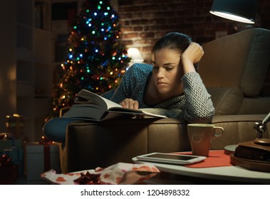 Woman Lying On The Sofa And Reading A Book She Received As Christmas Gift, She Has Just Unwrapped It