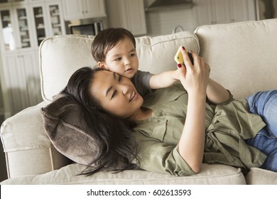 Woman lying on a sofa, smiling, cuddling with her young son and looking at a cell phone - Shutterstock ID 602613593