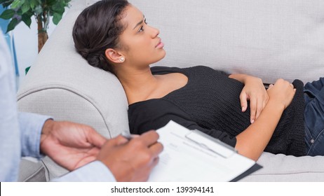 Woman Lying On Therapists Couch As Therapist Is Taking Notes
